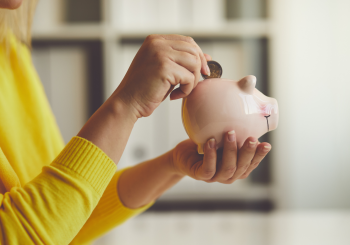 woman in yellow jumper putting coin into piggy bank